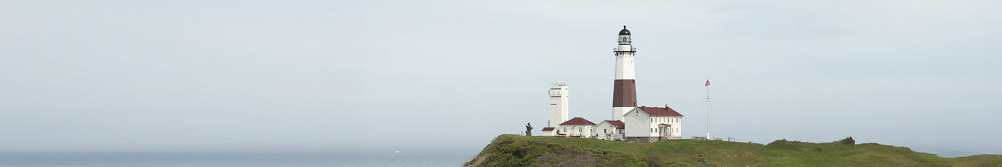 A panoramic view of the Montauk Point Lighthouse perched on a grassy cliff overlooking the ocean, under a soft overcast sky, evoking a coastal and historic charm.