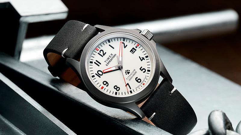A Timex Expedition wristwatch with a white dial, bold black Arabic numerals, and a date window at the 3 o’clock position. The watch features a red seconds hand, black hour and minute hands, and a logo above 6 o’clock indicating a collaboration with The North Face.