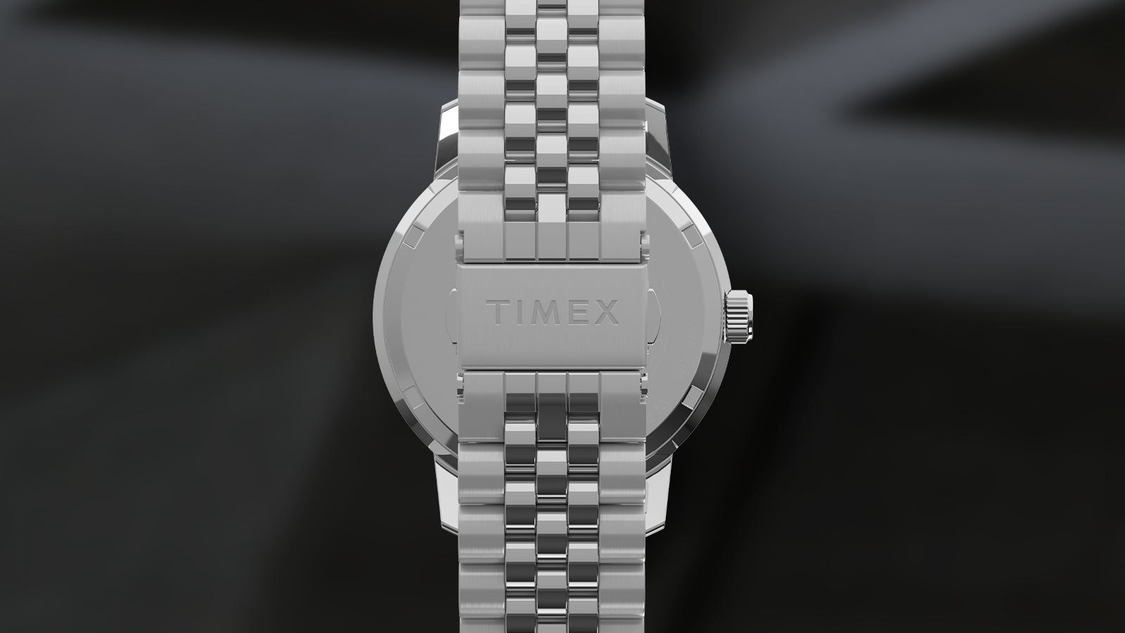 Rear view of the Timex Marlin® Quartz GMT highlighting the stainless-steel caseback and brushed clasp engraved with the “TIMEX” logo, attached to a multi-link stainless-steel bracelet, against a blurred dark background.