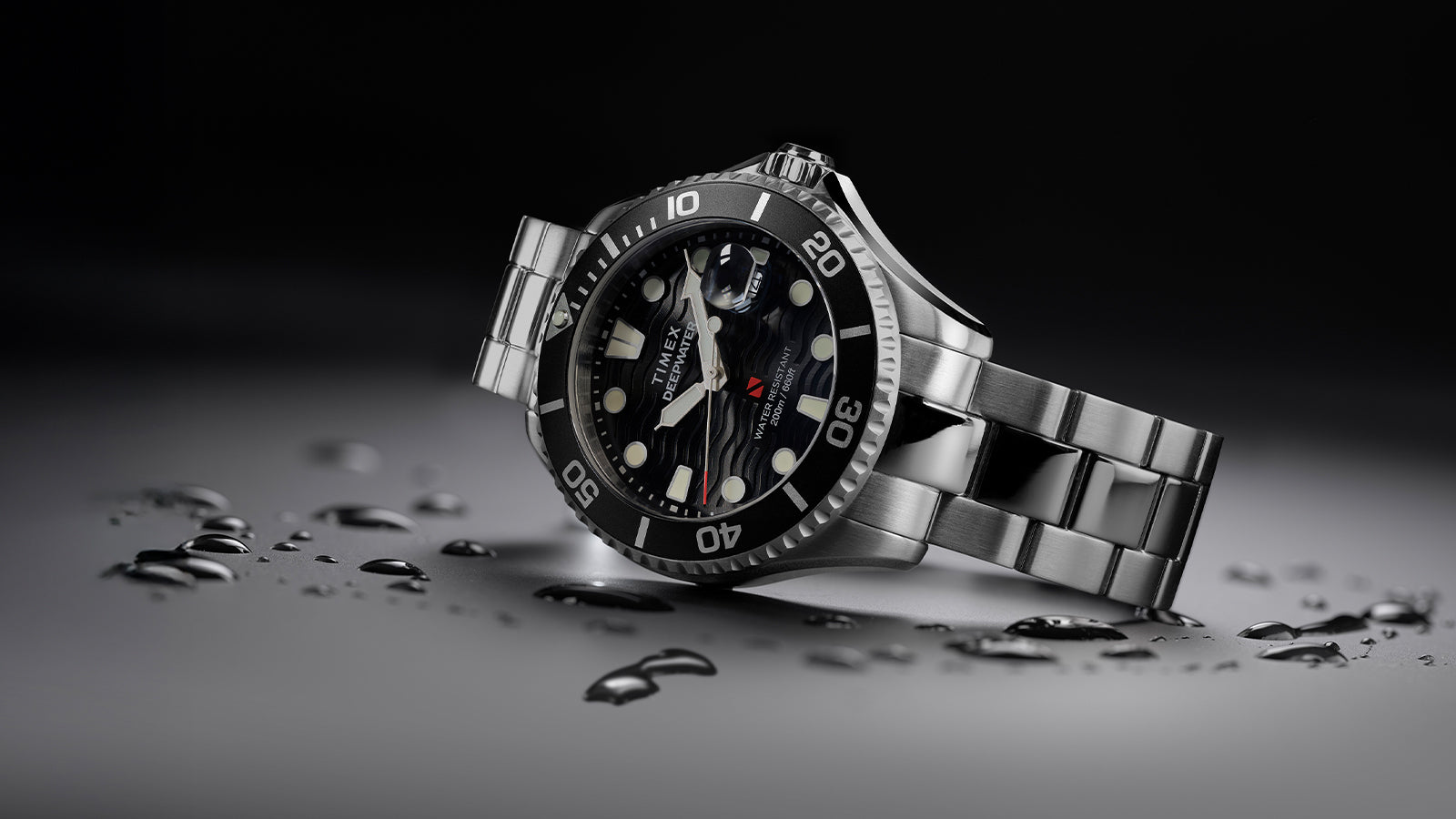 Timex Deepwater Meridian 200 dive watch in stainless steel with black rotating bezel and wavy black dial, lying at an angle with water droplets on the surface.