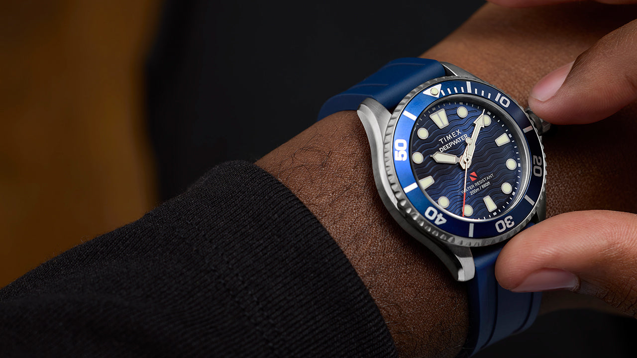 Close-up of a person wearing the Timex Deepwater Meridian 200 dive watch with a blue strap, adjusting the bezel.