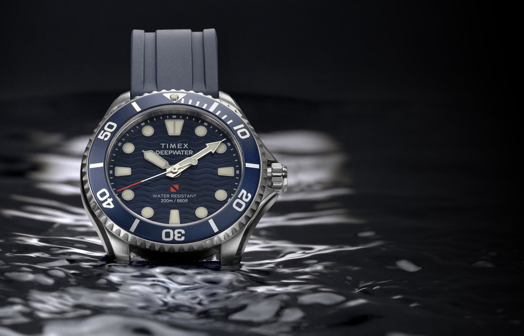 Timex Deepwater Meridian 200 with a blue strap and wave-pattern dial resting on the surface of dark water.