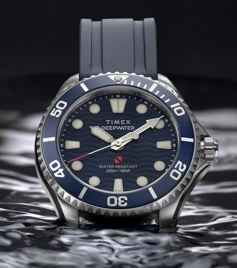 Timex Deepwater Meridian 200 with a blue strap and wave-pattern dial resting on the surface of dark water.