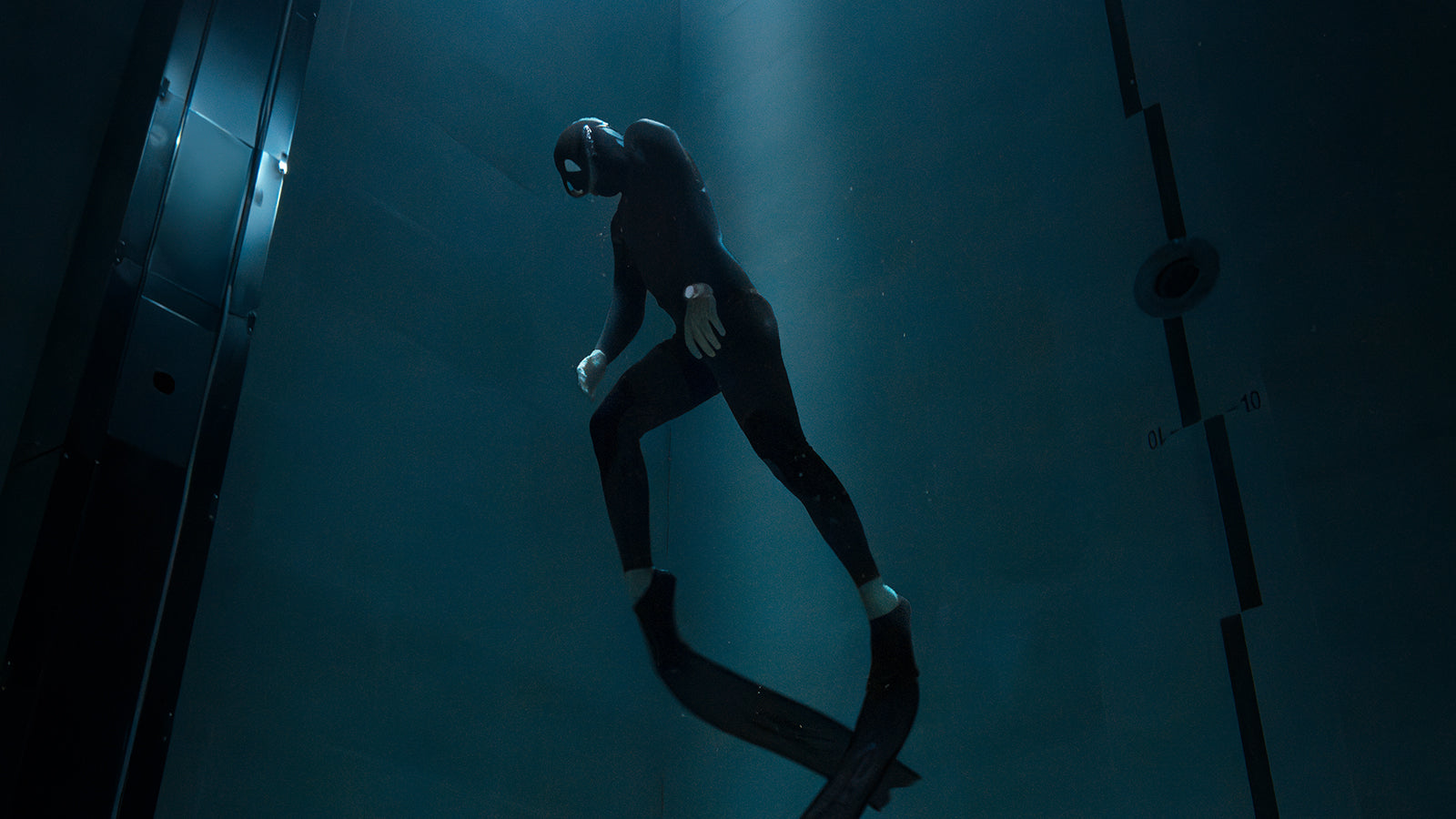 Freediver in a wetsuit illuminated by a beam of light underwater, wearing the Timex Deepwater Meridian 200 dive watch while floating upward in the deep.