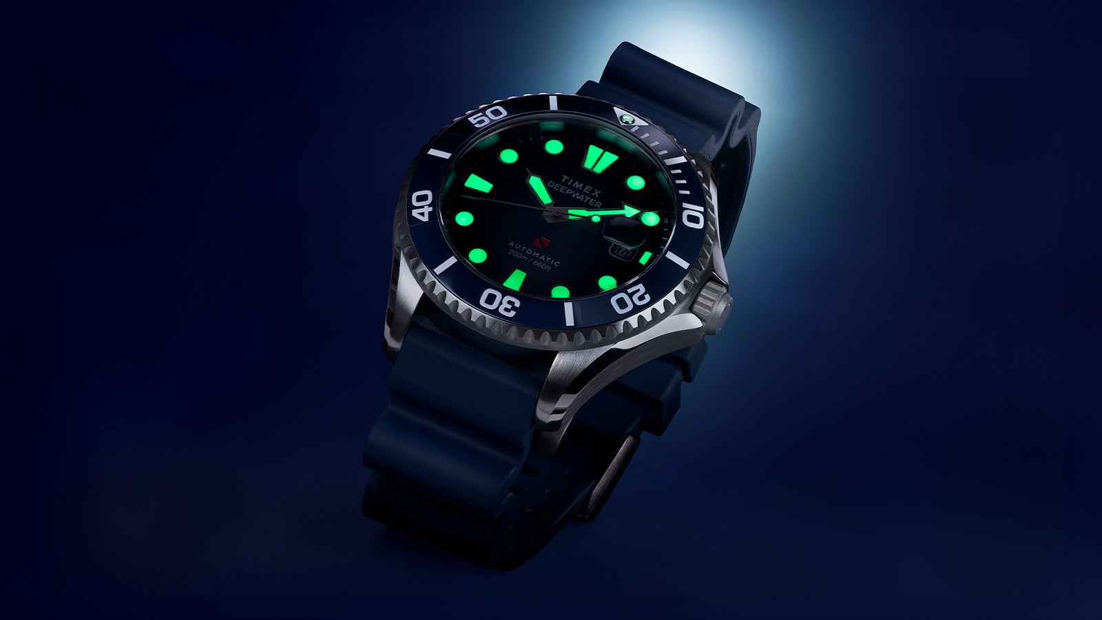 Close-up of the Timex Deepwater Meridian 200 automatic dive watch with luminous markers glowing green against a dark blue background.