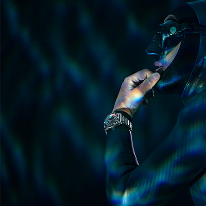 Side profile of a diver adjusting wetsuit hood under shimmering water light, wearing the Timex Deepwater Meridian 200 on a metal bracelet.