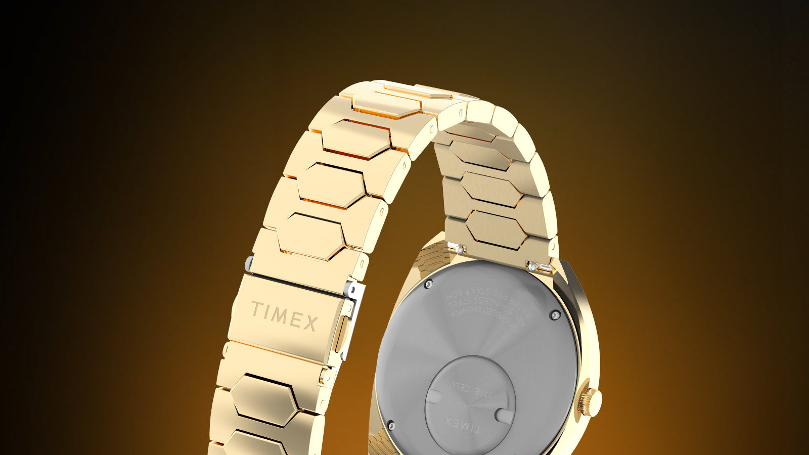 Rear view of the Q Timex® 1972 Time Machine Reissue gold-tone watch showing the stainless-steel caseback engraved with specifications, gold-tone hexagonal-link bracelet, and clasp engraved with the “TIMEX” logo, against a warm amber gradient background.