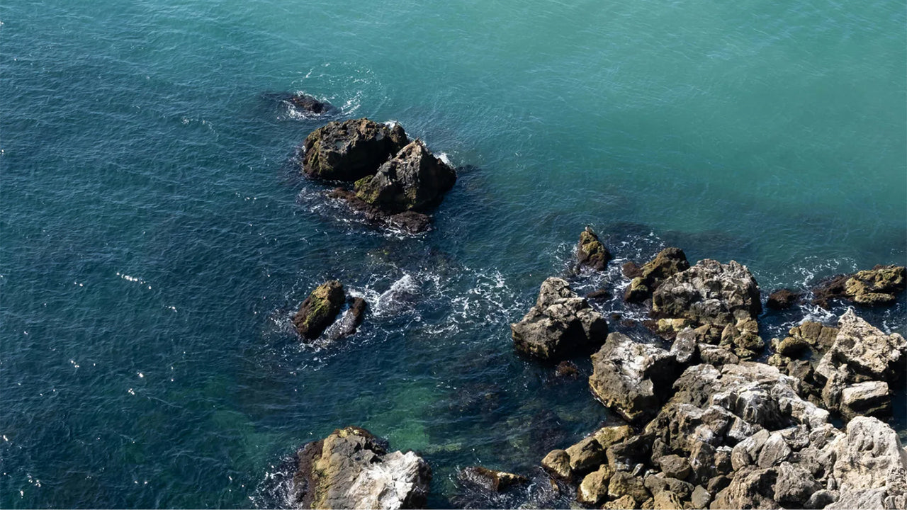 Aerial view of rocky shoreline with ocean waves splashing against the rocks, symbolizing outdoor adventure.