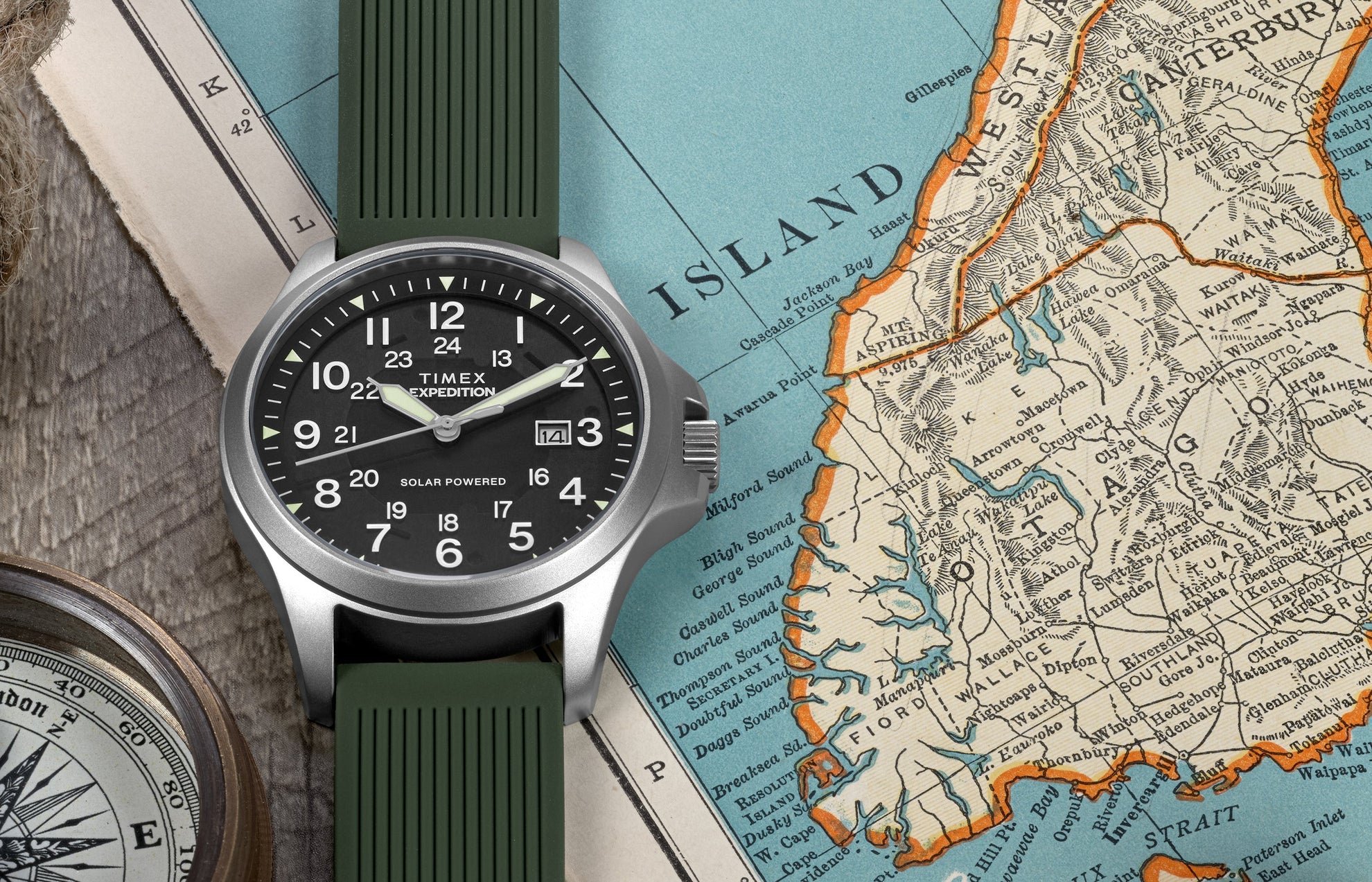 A Timex Expedition® Field Post Solar watch with green strap rests on an old map, paired with a compass, symbolizing exploration.