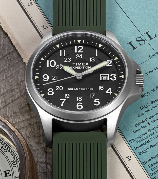 A Timex Expedition® Field Post Solar watch with green strap rests on an old map, paired with a compass, symbolizing exploration.