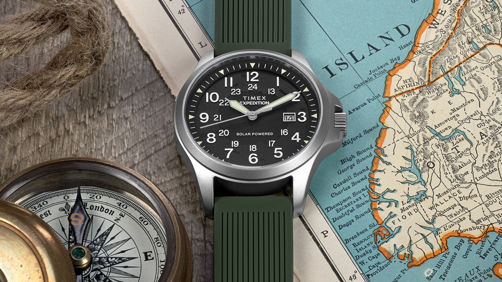 A Timex Expedition® Field Post Solar watch with green strap rests on an old map, paired with a compass, symbolizing exploration.
