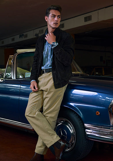 Model leaning on a classic blue convertible wearing a Q Timex® Chronograph with white dial, navy tachymeter bezel, and stainless-steel bracelet.