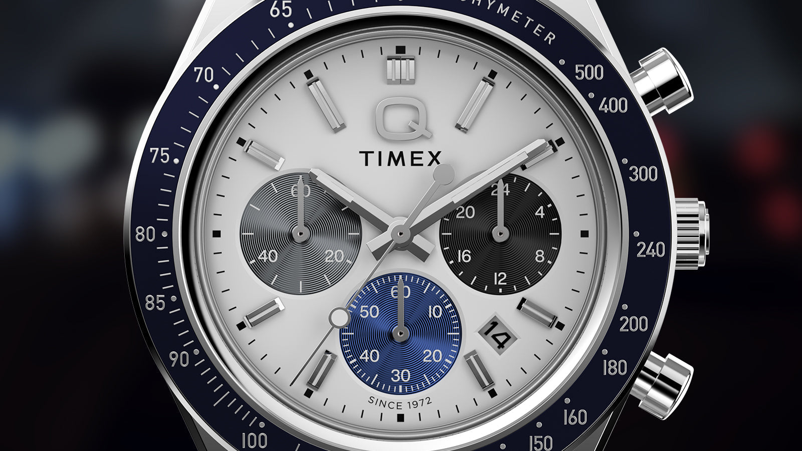 Macro of the Q Timex® Chronograph dial—white face, gray and black sub-dials with blue 6 o’clock sub-dial, navy tachymeter scale, and date at 4 o’clock.