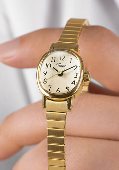 Close-up of a Timex Cavatina Mini gold-tone watch with white dial and black Arabic numerals, held delicately in hand.
