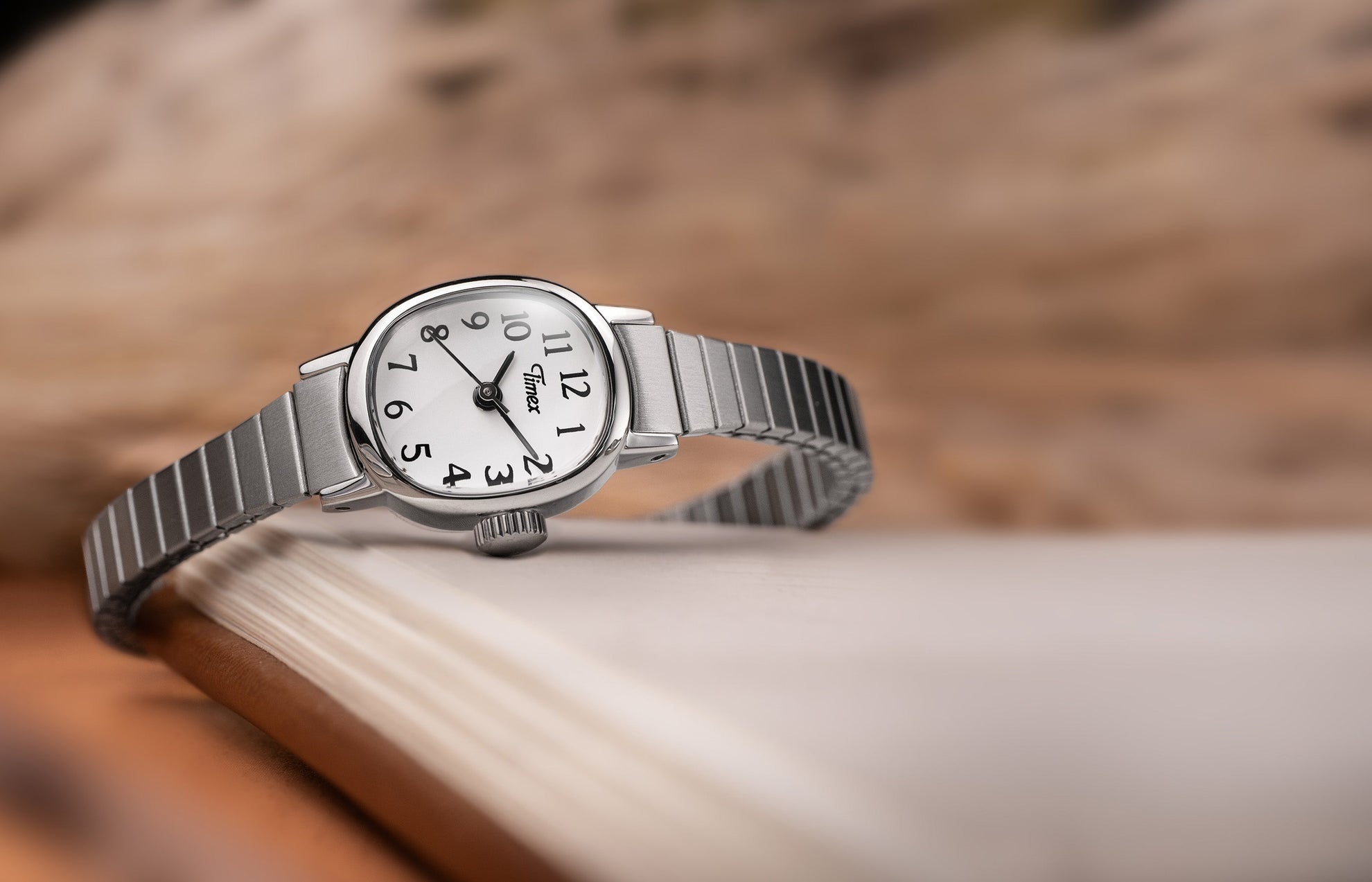 Timex Cavatina Mini watch with a silver expansion bracelet and white dial resting elegantly on the edge of an open book.