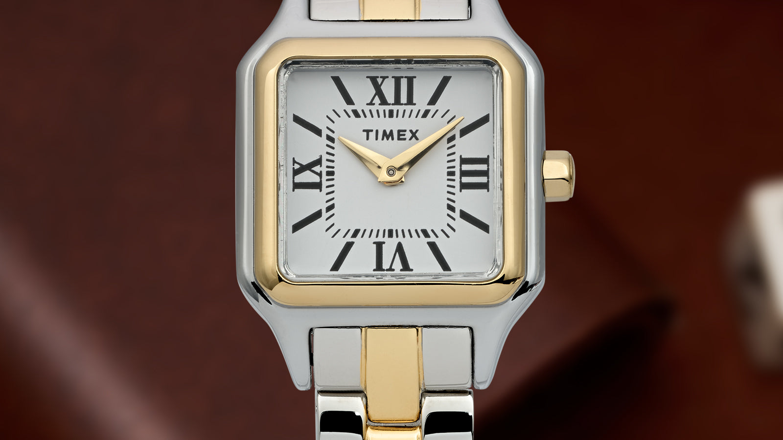 Close-up of the Timex Legacy Addison two-tone square watch showing white dial with black Roman numerals, gold hands, and bi-color link bracelet.