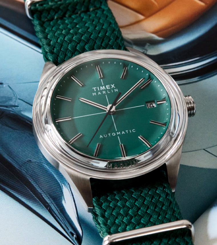 Timex Marlin® Jet Automatic watch with a green sunray dial, stainless-steel case, and woven green fabric strap, displayed on an open magazine background.