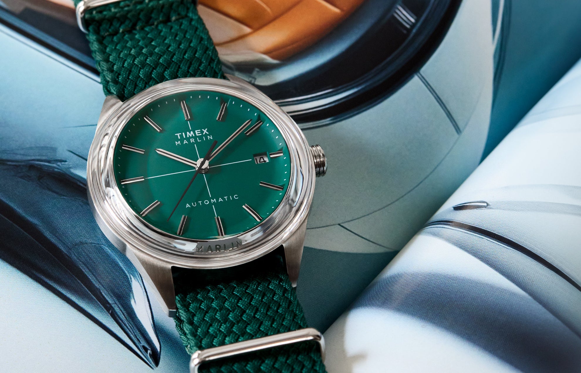 Timex Marlin® Jet Automatic watch with a green sunray dial, stainless-steel case, and woven green fabric strap, displayed on an open magazine background.