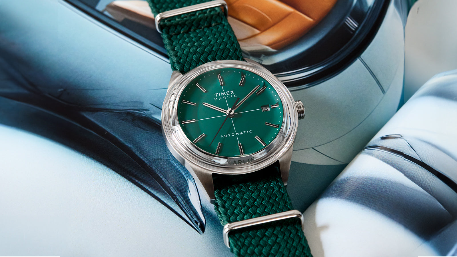 Timex Marlin® Jet Automatic watch with a green sunray dial, stainless-steel case, and woven green fabric strap, displayed on an open magazine background.