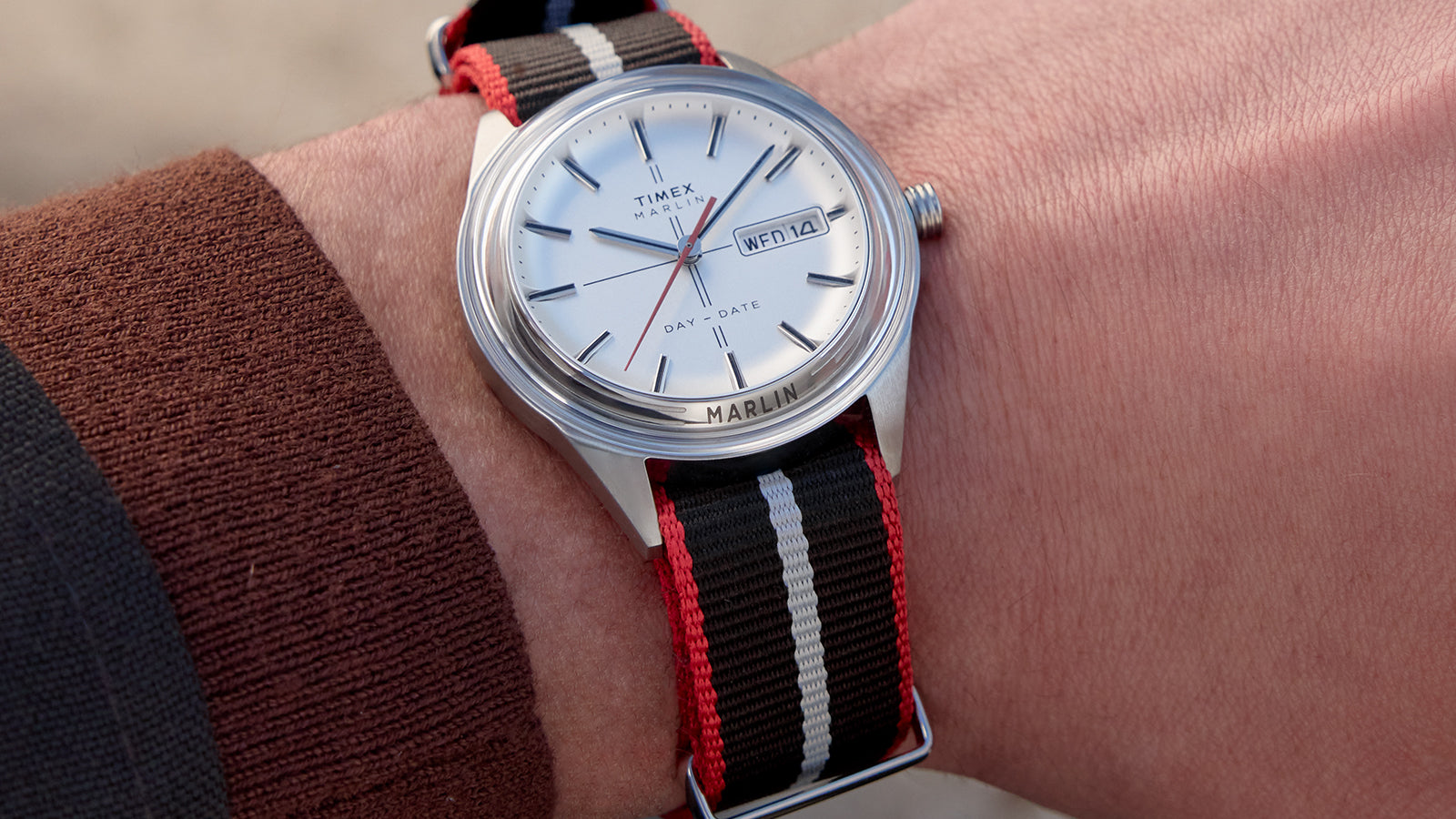 Timex Marlin® Jet Quartz watch worn on wrist, showing its polished case, clean silver dial, and bold red-and-black striped strap.