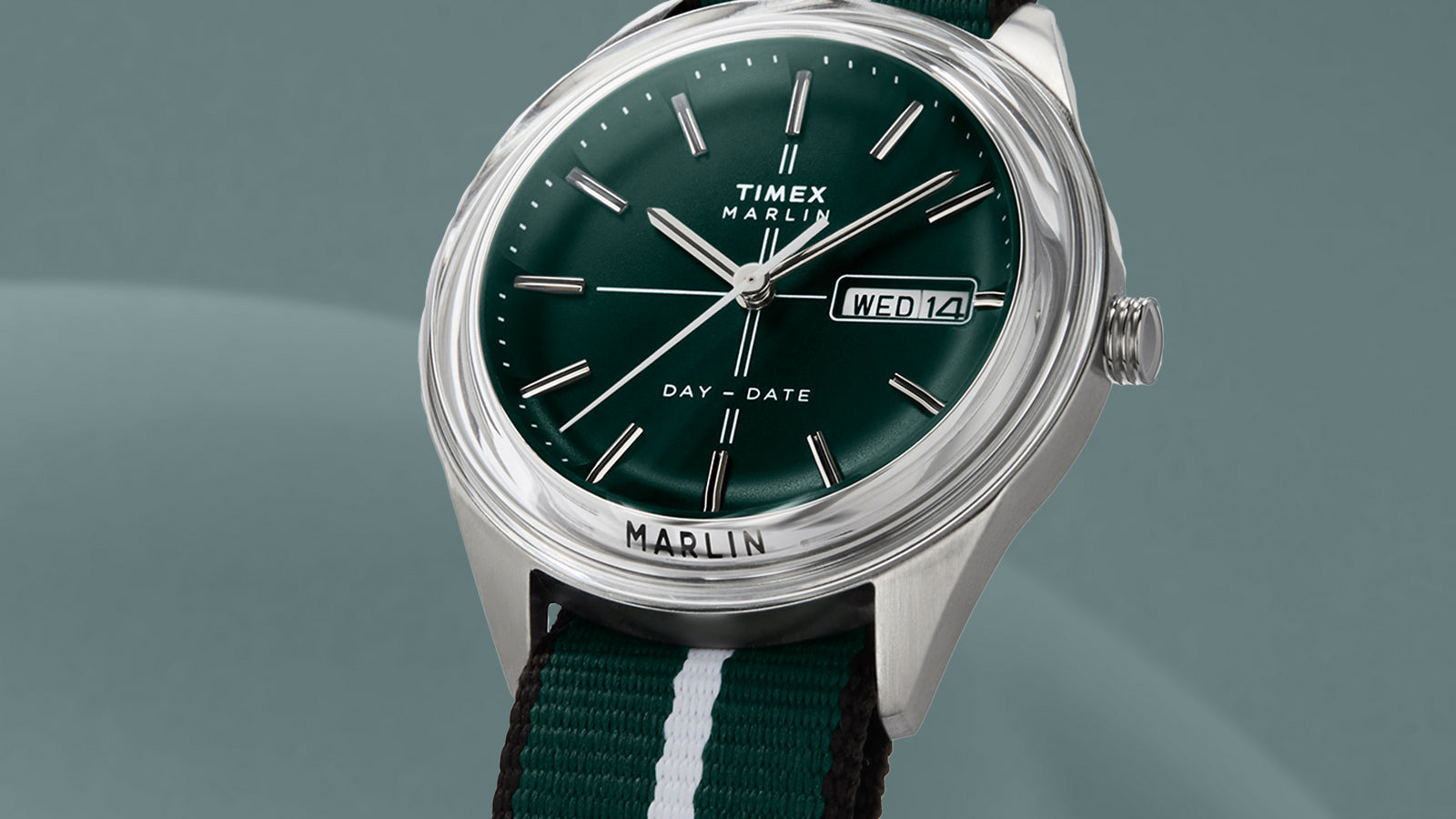 Timex Marlin® Jet Quartz watch on a plain teal background, showing polished stainless-steel case, domed crystal, green dial, and striped green-and-white fabric strap.