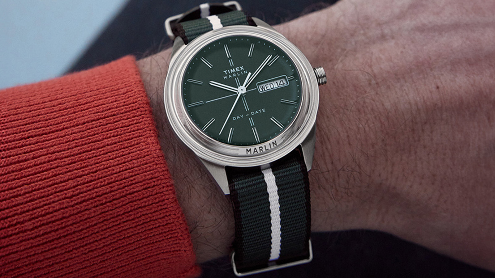 Timex Marlin® Jet Quartz watch worn on wrist, featuring a green dial with day-date display and a striped green-and-white nylon strap.