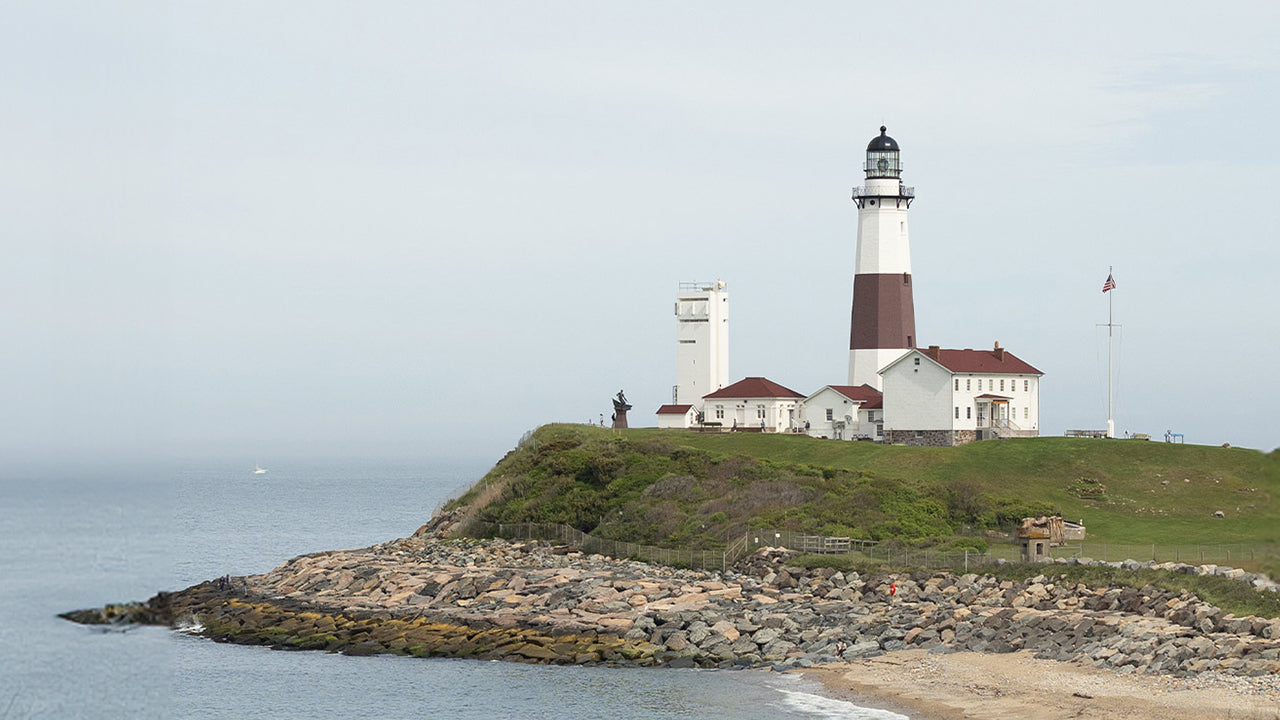 Coastal lighthouse on a grassy bluff above rocky shoreline, suggesting a classic New England setting.