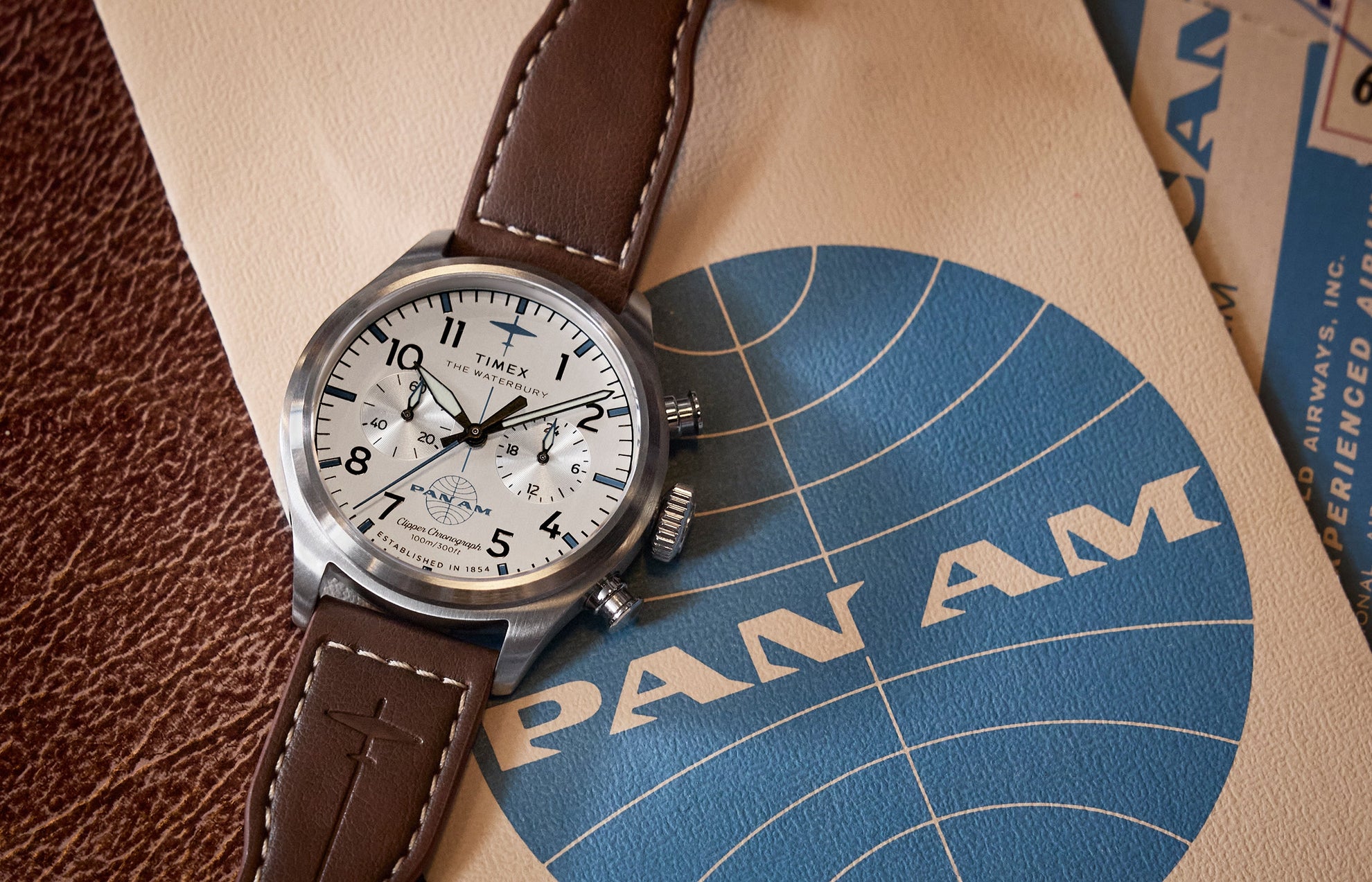 Close-up of the Timex x Pan Am® Waterbury Ace Chronograph with a white dial, black numerals, and brown leather strap resting on vintage Pan Am travel documents.