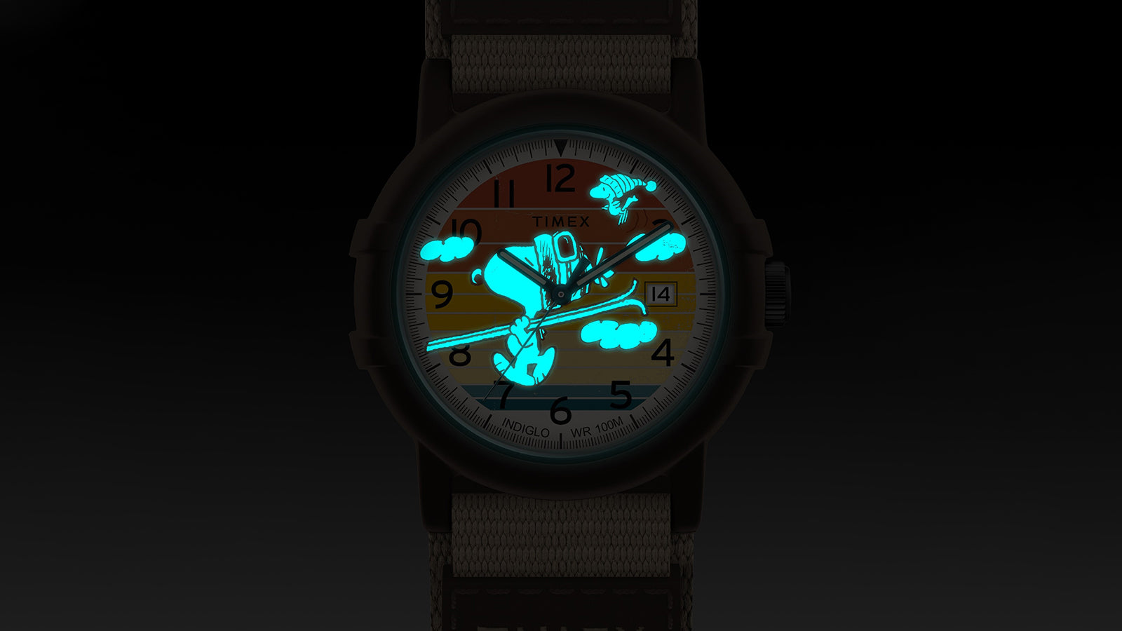 Timex x Peanuts® Camper Ski watch glowing with blue-green INDIGLO® backlight, illuminating Snoopy skiing on the vibrant dial against a dark background.