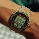 A person wearing the TIMEX® IRONMAN® Flix x Huckberry on their wrist outdoors, highlighting the durable design and clear digital display. The beige strap with orange branding contrasts with the watch’s rugged case.