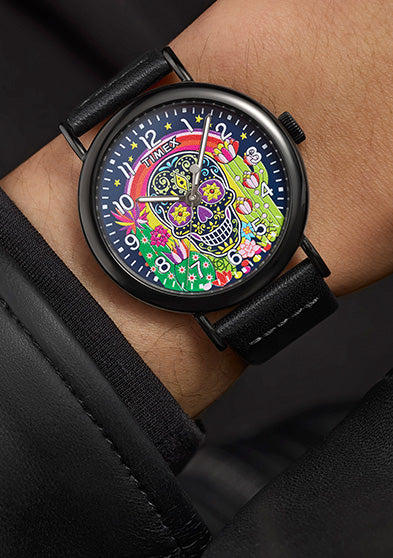 Timex Weekender Day of the Dead watch on wrist, with black leather strap and vibrant sugar skull dial design visible against a black jacket cuff.