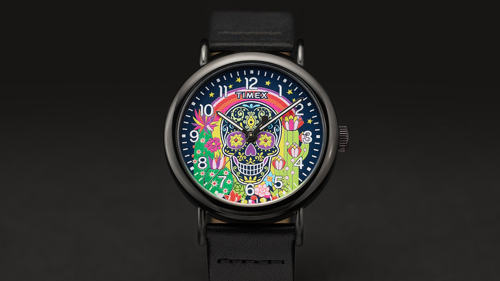Timex Weekender Day of the Dead watch front view showing the colorful sugar skull dial with rainbow, cactus, and flower motifs, paired with a black leather strap.