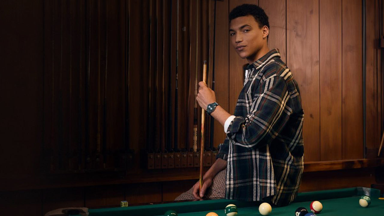 Model wearing the Timex Waterbury Heritage Chronograph in a wood-paneled billiards room, holding a cue stick, showcasing the sporty and vintage-inspired design.