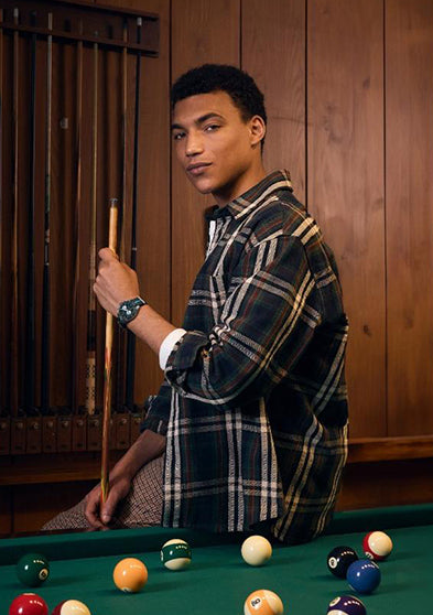 Model wearing the Timex Waterbury Heritage Chronograph in a wood-paneled billiards room, holding a cue stick, showcasing the sporty and vintage-inspired design.