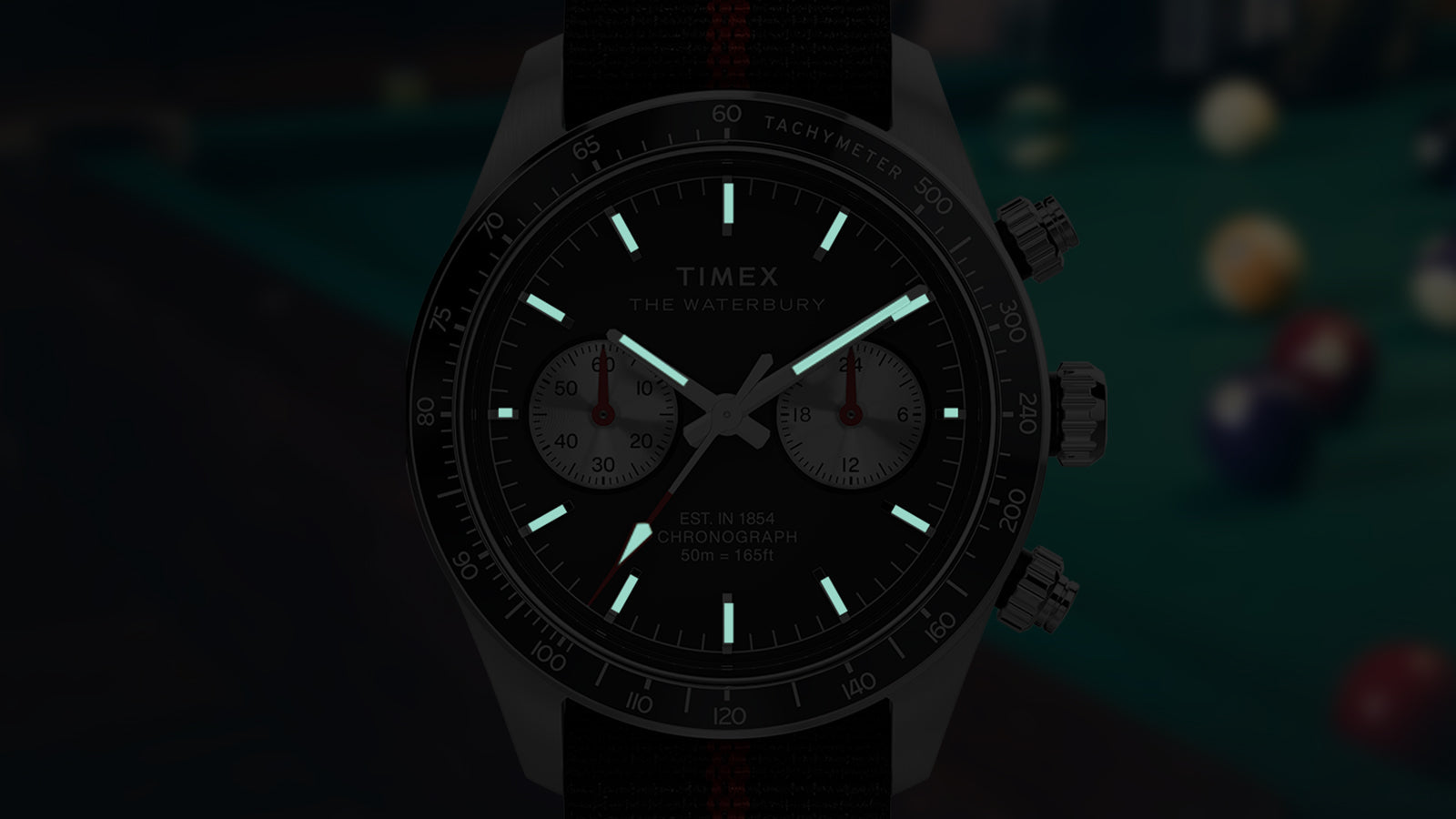 Timex Waterbury Heritage Chronograph with INDIGLO® backlight, glowing hour markers and hands against a dark background.