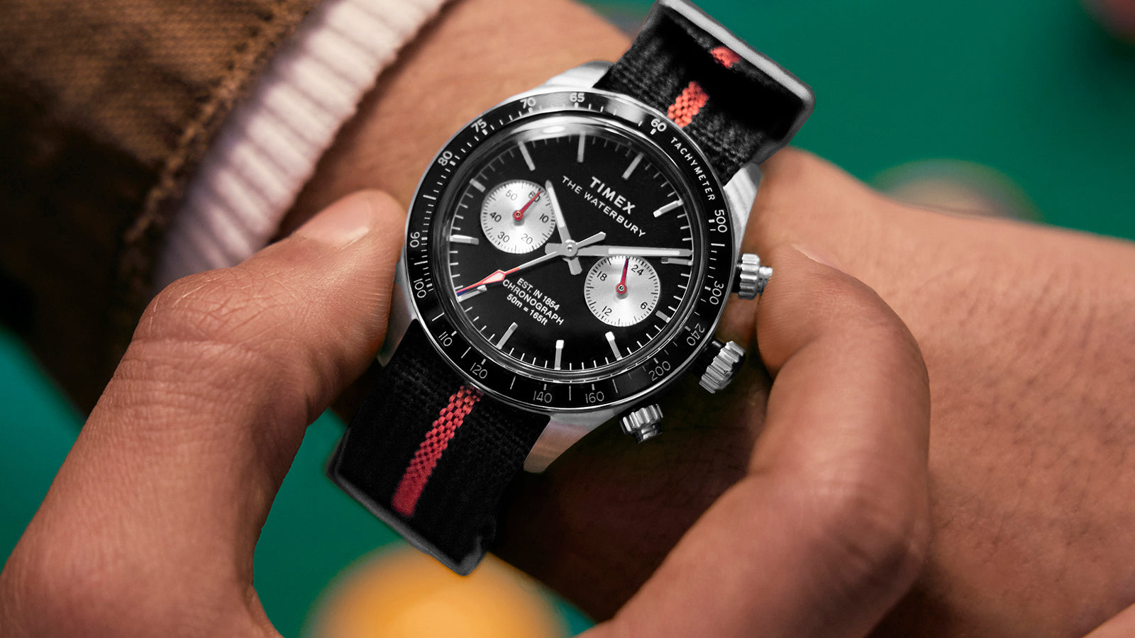 Person adjusting the Timex Waterbury Heritage Chronograph on wrist, emphasizing the sleek design and sport-inspired strap.