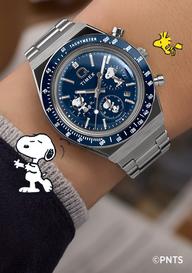Person wearing the Timex x Peanuts® Q Timex® Chronograph featuring Snoopy and Woodstock on a blue dial with stainless steel bracelet. The playful Peanuts® illustrations complement the watch’s refined, retro-inspired chronograph design.