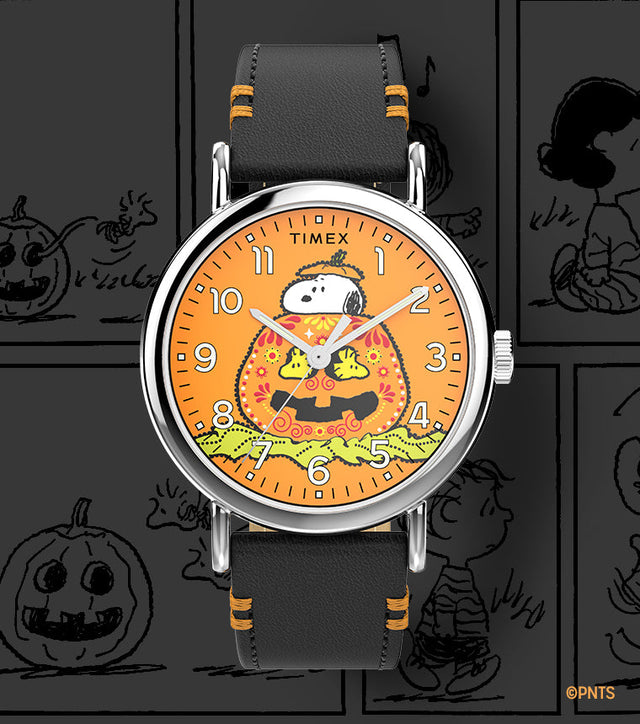 Timex x Peanuts® Weekender watch with Snoopy resting on a jack-o’-lantern against an orange dial. Black leather strap with orange stitching, set on a Peanuts Halloween comic strip background.
