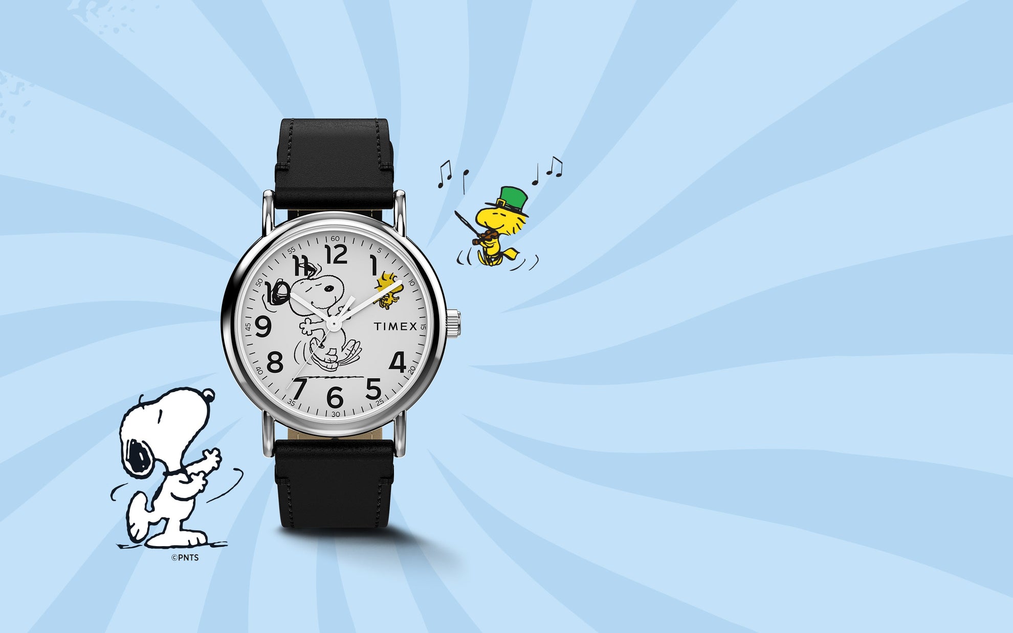 Timex x Peanuts® Weekender watch with a white dial featuring Snoopy dancing with Woodstock, displayed on a light blue background with playful Peanuts® illustrations. The watch has a black leather strap and classic silver-tone case.