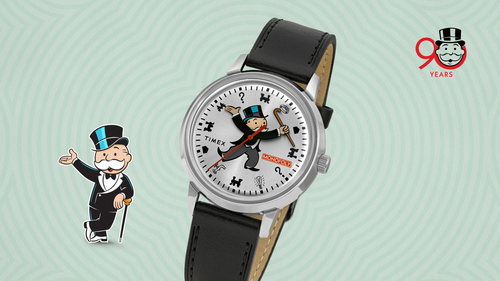 Angled front view of the Timex x Monopoly Marlin® Automatic watch, showing the Monopoly mascot illustration across the dial. The watch features a polished stainless-steel case, red Monopoly logo, and black leather strap with tan lining. The Monopoly 90 Years logo appears in the background.