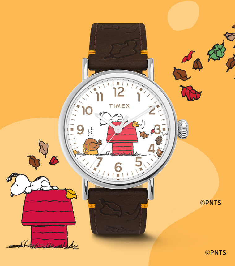 Timex x Peanuts® Standard Thanksgiving Edition watch displayed next to a Snoopy and Woodstock illustration surrounded by colorful falling leaves, celebrating a cozy fall theme.