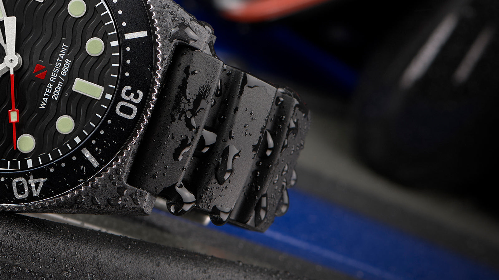 Close-up detail of the Timex Deepwater watch showing the black silicone strap covered in water droplets and part of the black dial with luminous markers, red seconds hand, and the 200m/660ft water resistance marking.