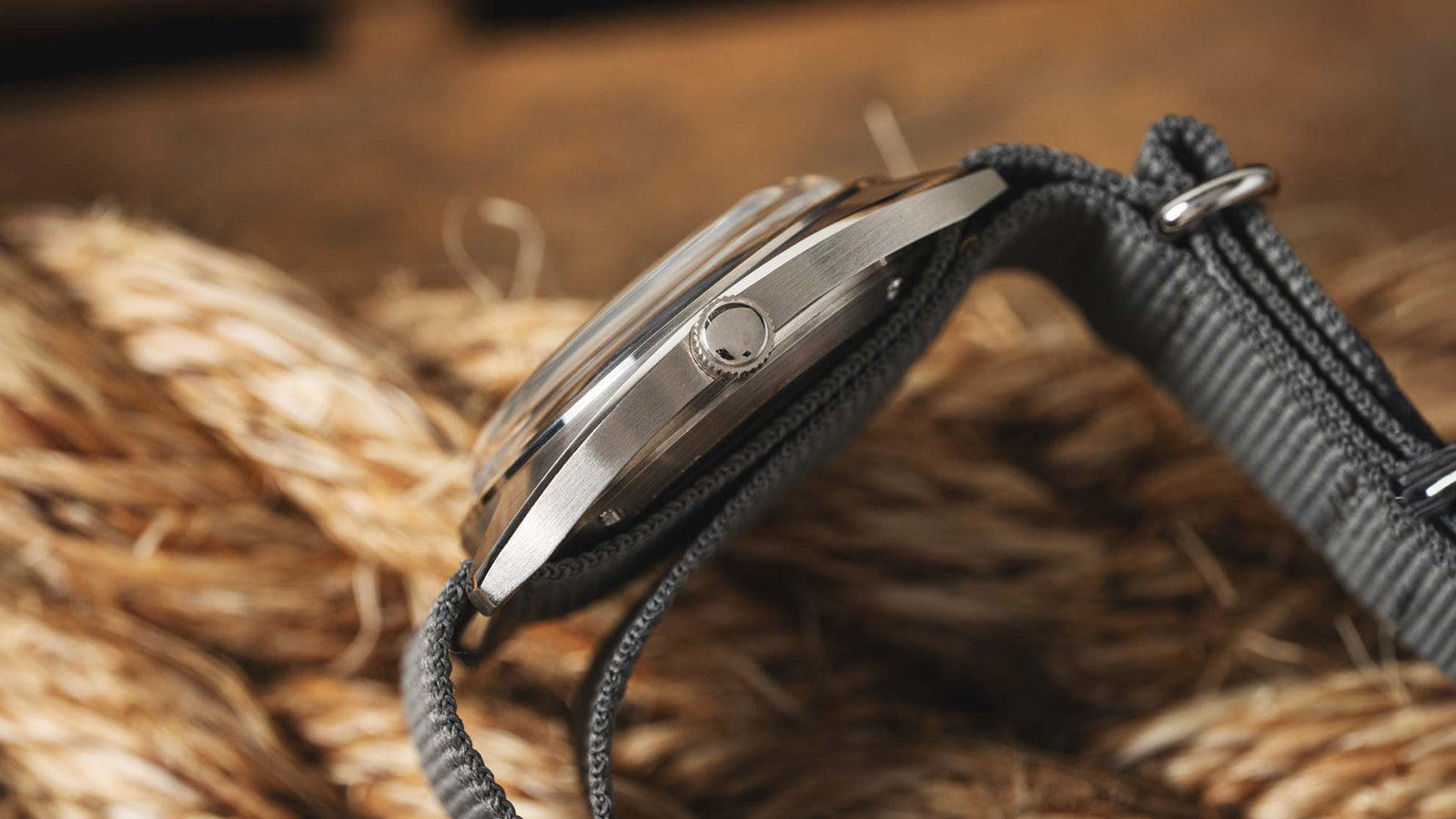 A detailed view of the Timex x Worn & Wound Storm dial on a dark textured surface, showing the layered gray and silver tones, blue minute track, and red TIMEX logo.