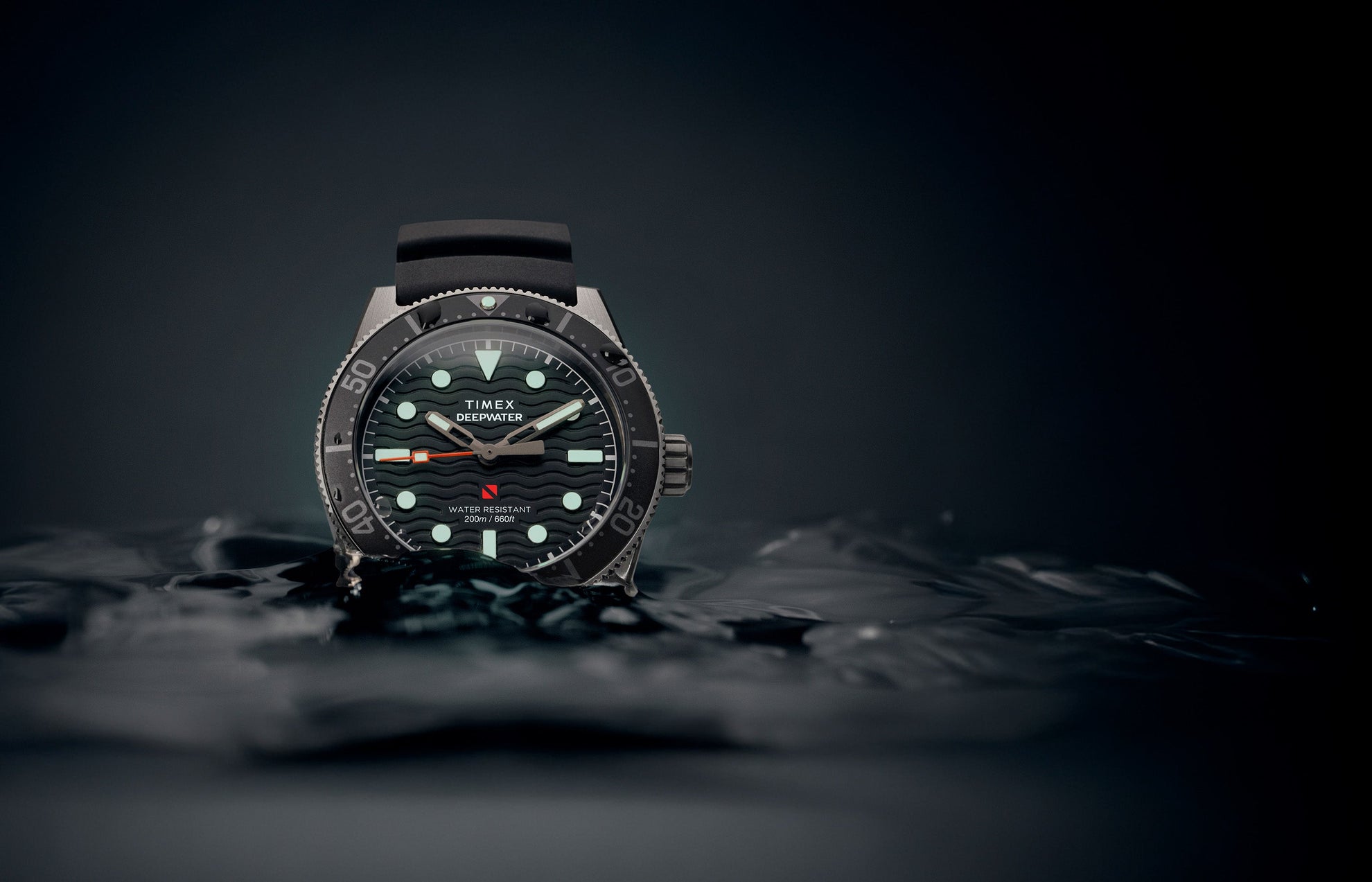 Timex Deepwater Reef 200 dive watch emerging from dark water, featuring a black dial with luminous markers and hands, black rubber strap, and 200-meter water resistance rating.