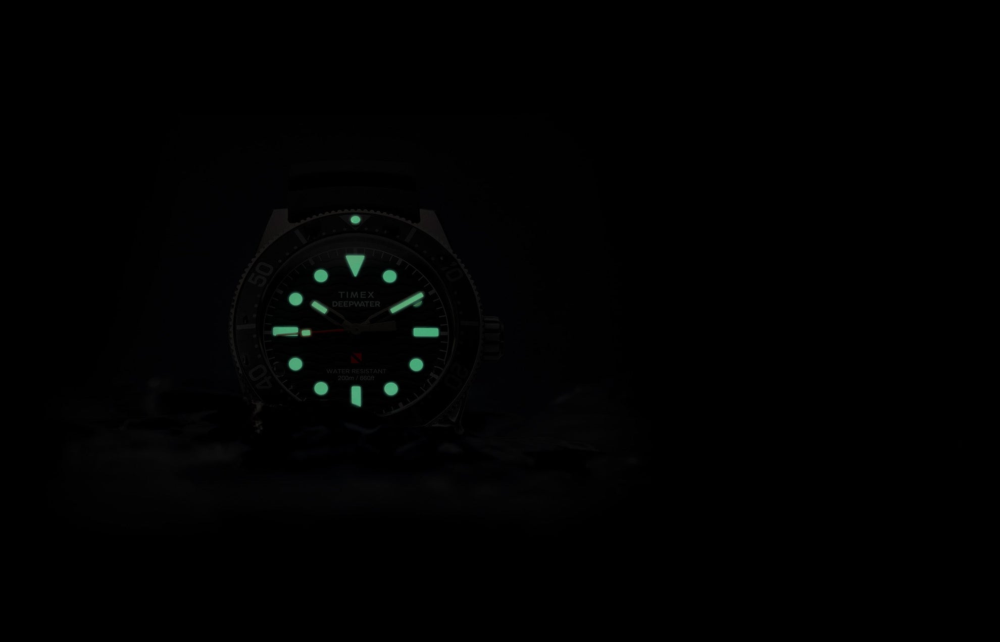 Timex Deepwater Reef 200 watch glowing in darkness, with bright green lume on the hands and hour markers, emphasizing superior underwater visibility.