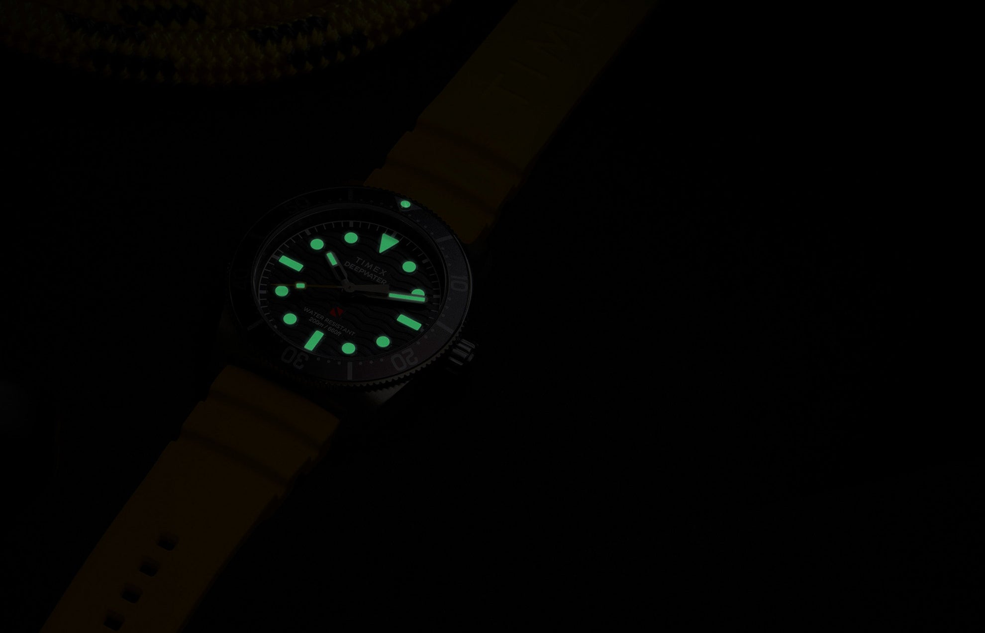 Timex Deepwater Reef 200 dive watch glowing in the dark, showing luminous hands and hour markers for enhanced underwater visibility.