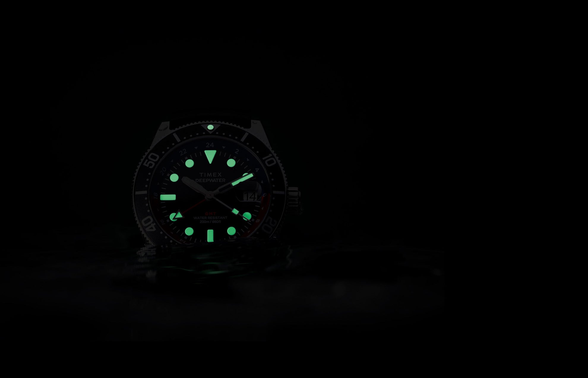 Timex Deepwater Reef 200 GMT glowing in darkness, showing bright green luminescent markers and hands for underwater visibility.