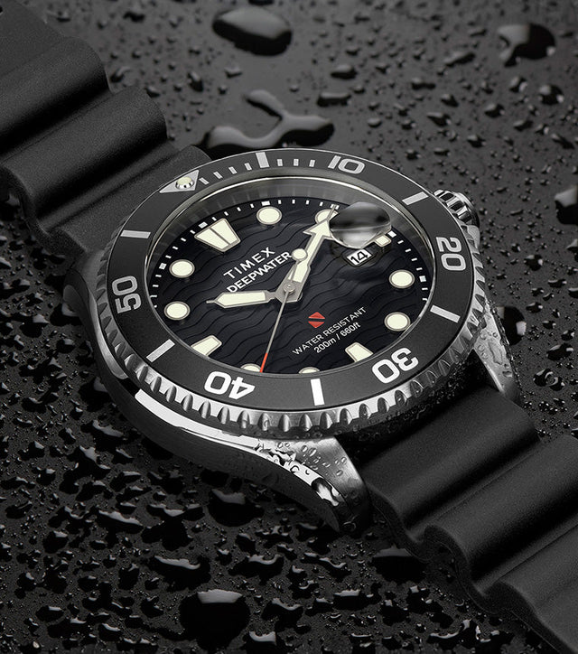 Timex Deepwater Meridian 200 dive watch with black strap and wave-textured black dial resting on a surface covered in water droplets, emphasizing its 200-meter water resistance and rugged construction.