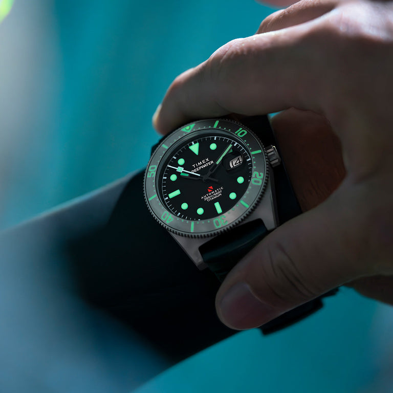 Diver wearing the Timex Deepwater Reef 200 Titanium Automatic underwater, watch dial glowing with bright green lume, emphasizing legibility in low light.