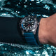 Diver wearing the Timex Deepwater Reef 200 watch underwater, the blue strap and stainless steel case reflecting light as bubbles rise around them.